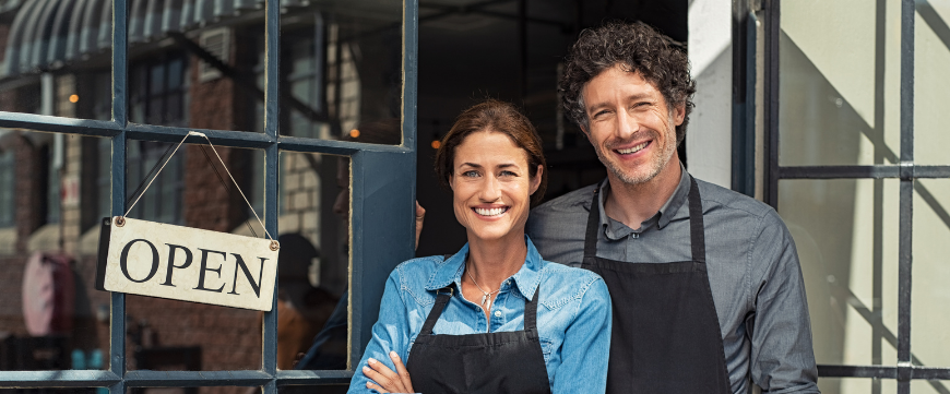 Man and woman in aprons outside coffee shop with "open" sign on window