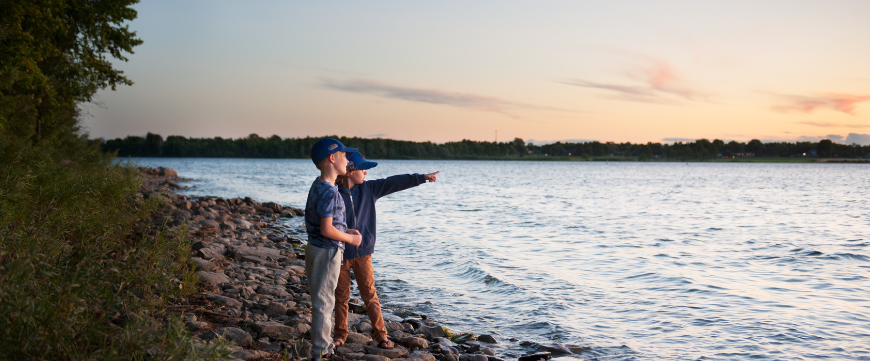 Two boys standing on waterfront pointing in the distance